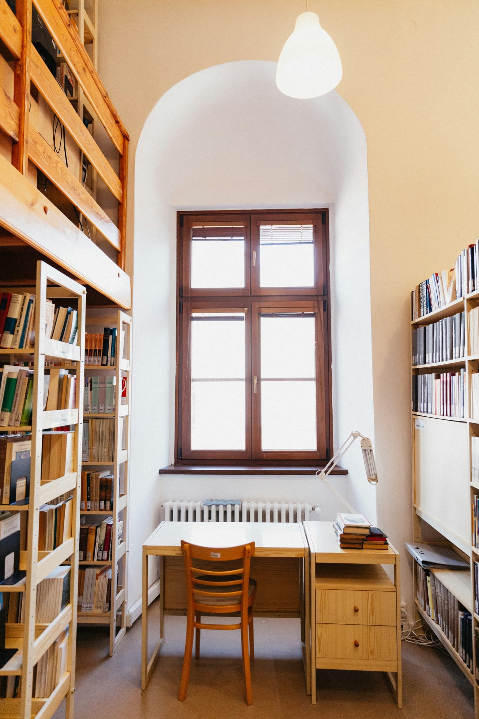 A desk and chair beneath a tall window, framed by library shelves